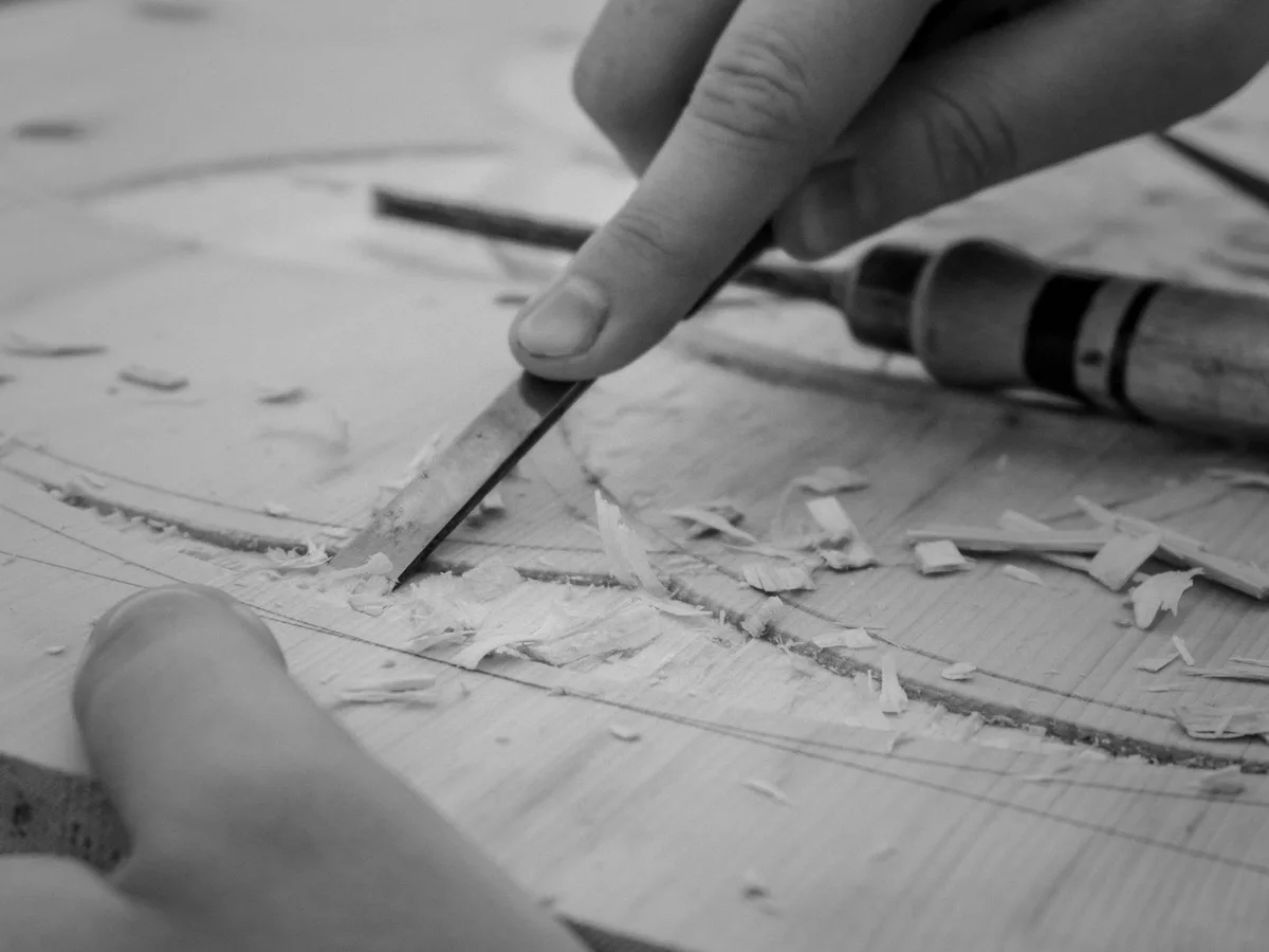 Hands carving a curve into a board with a chisel