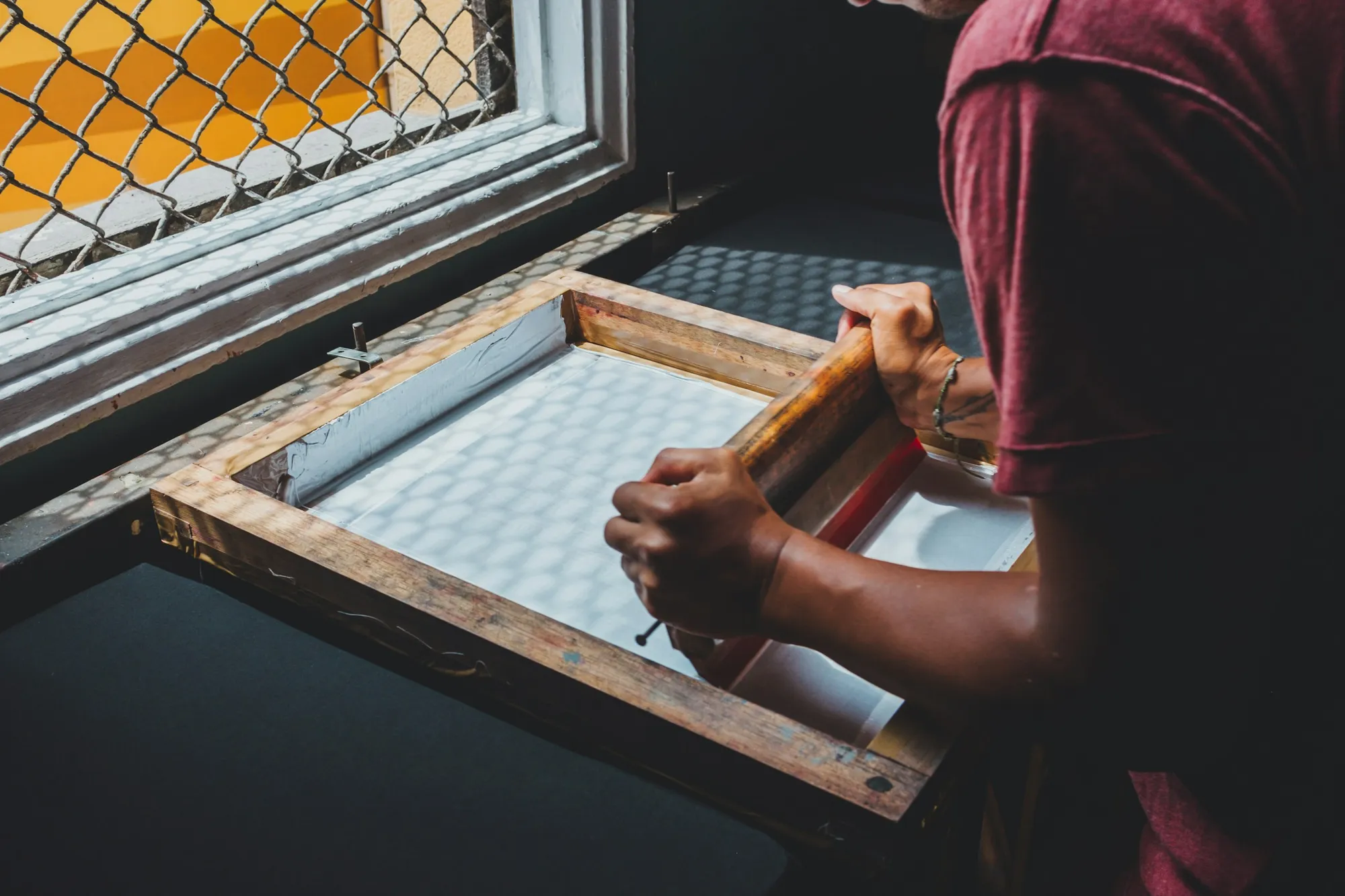 Hands pulling a screen print by a workshop window